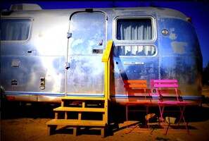 A vintage camper van with a sliding door, a small window, and a ramp leading to a foldable chair. - Charming Riverfront Airstream Rental for Getaway near Fredericksburg, Texas (Mason)