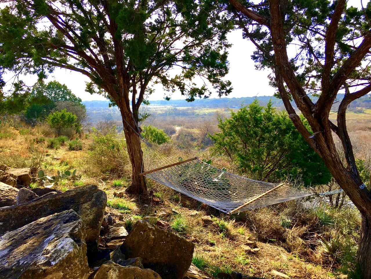 Een hangmat tussen bomen in een natuurlijke omgeving, met uitzicht op het landschap.