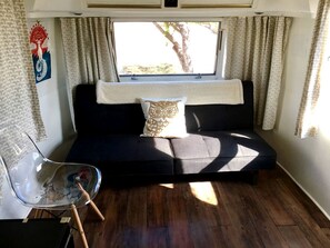 Um espaço de estar compacto com sofá, poltrona transparente e janela.