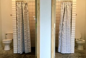 Casa de banho com duas sanitas, um separador de chuveiro e paredes em azulejo.