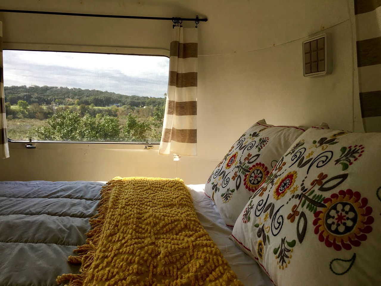 Een slaapkamer met een bed, een raam met gordijnen en uitzicht op groen buiten.