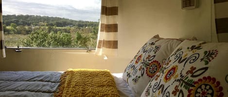 A bedroom with a bed, a window with curtains, and a view of greenery outside.