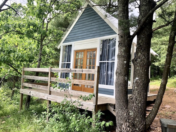 A small cabin with a wooden deck, a front door, and large windows.