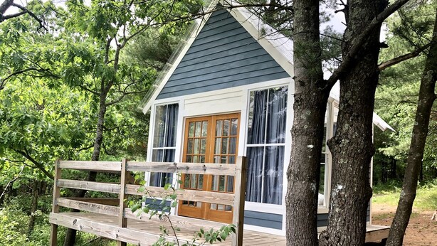 Una cabaña pequeña con terraza de madera, puerta principal y ventanas amplias.