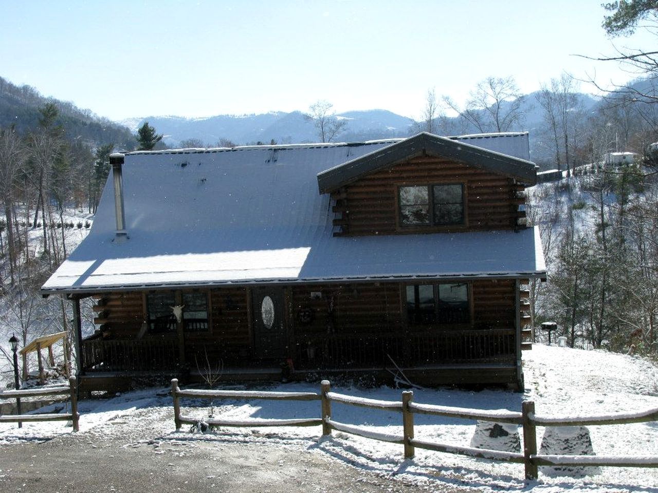 A log cabin with a porch, surrounded by snow-covered ground and trees.