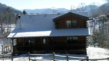 A log cabin with a porch, surrounded by snow-covered ground and trees.