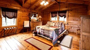 A wooden cabin bedroom with a bed, a desk, a chair, and a wardrobe.