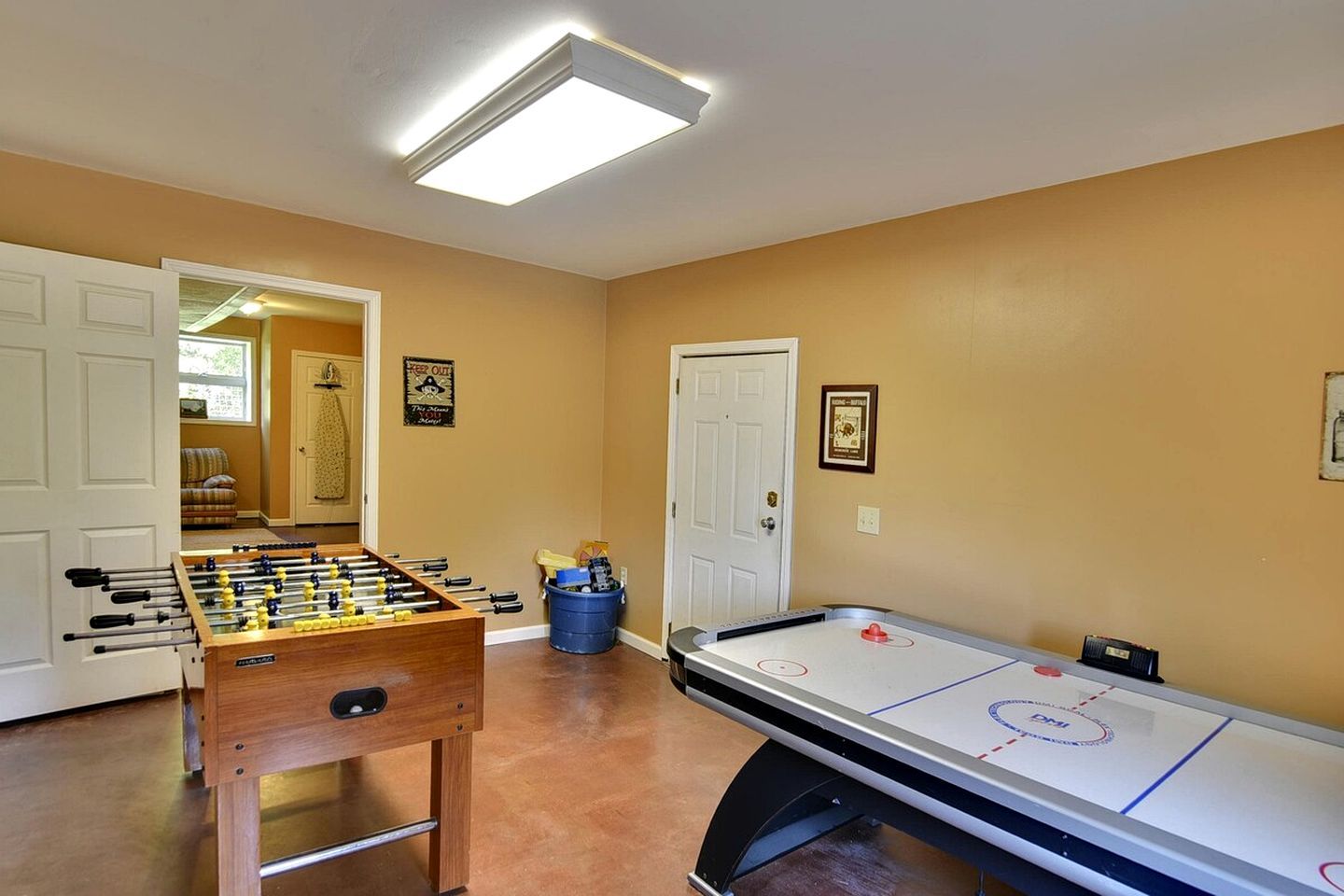 A room with a foosball table and an air hockey table, with a door leading to another room.