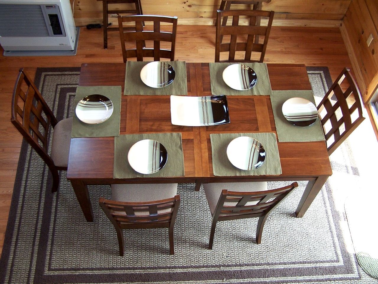 Un tavolo da pranzo in legno con sei sedie, ognuna con un sottopiatti riflettente.