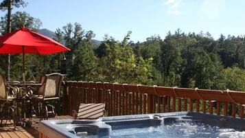 Un jacuzzi en una terraza de madera con un paraguas rojo, rodeado de sillas y una valla de madera.