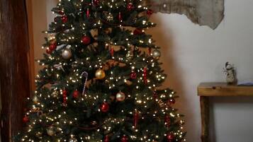 A Christmas tree with lights and ornaments, a clock, and a wooden wall with a bear painting.
