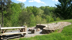 A picnic area with benches and a fire pit surrounded by a gravel path.