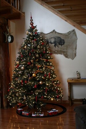 A Christmas tree with lights and ornaments, a clock, and a wooden wall with a bear painting. - Charming Cabin Rental with a Hot Tub and Fireplace in the Smoky Mountains (Clyde)