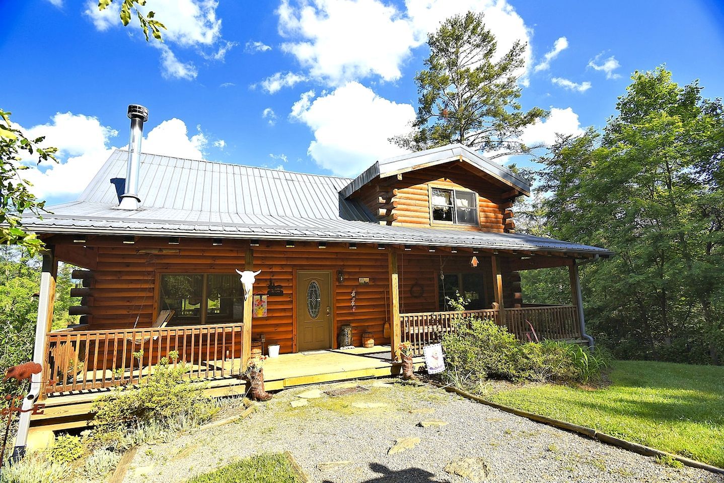 A log cabin with a porch, a chimney, and a grassy yard.