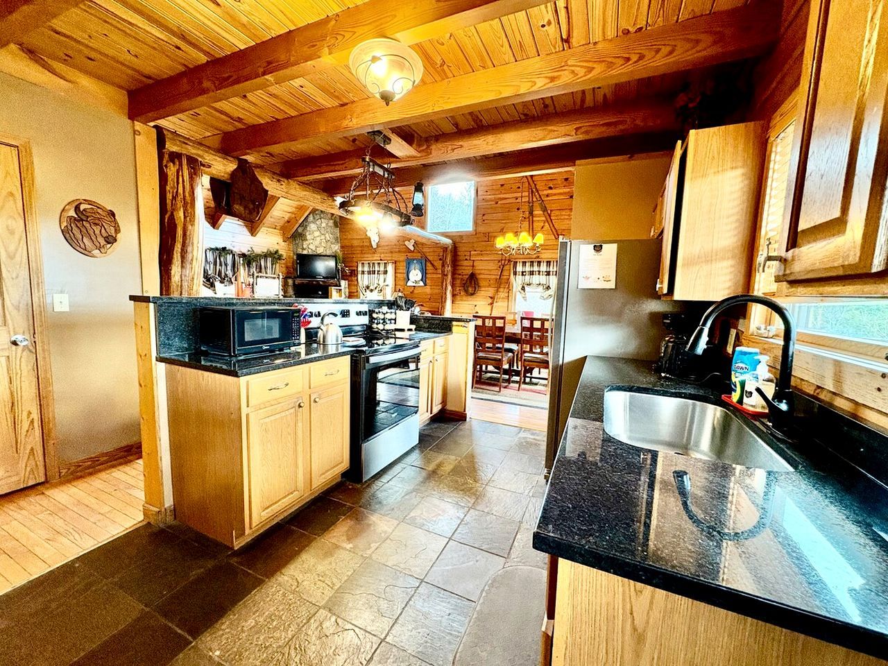 A kitchen with wooden cabinets, a black countertop, a stove, and a sink.