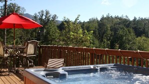 A hot tub on a wooden deck with a red umbrella, surrounded by chairs and a wooden fence.