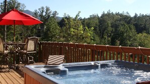 Un jacuzzi en una terraza de madera con un paraguas rojo, rodeado de sillas y una valla de madera.