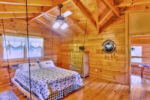 A wooden cabin bedroom with a bed, a ceiling fan, a dresser, and a wall decoration. - Charming Cabin Rental with a Hot Tub and Fireplace in the Smoky Mountains (Clyde)
