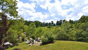 Un espacio al aire libre con césped, una chimenea y sillas Adirondack, rodeado de árboles y un paisaje ondulado.