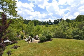 Eine begrünte Außenanlage mit Feuerstelle und Adirondack-Stühlen, umgeben von Bäumen und einer hügeligen Landschaft.