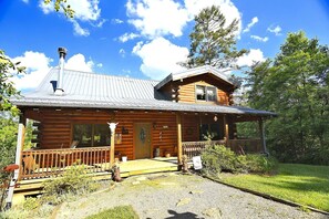 A log cabin with a porch, a chimney, and a grassy yard. - Charming Cabin Rental with a Hot Tub and Fireplace in the Smoky Mountains (Clyde)
