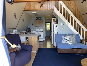 A compact living space with a kitchenette, a sofa, a dining area, and a staircase. - The Eagles Nest (Ellsworth)