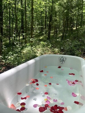 A bathtub filled with water and rose petals, surrounded by a forest. - Charming Vacation Rental in a Barn on a Horse Farm near Afton Mountain in Virginia (Afton)