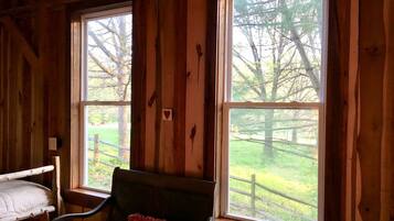 A wooden cabin room with two large windows, a bunk bed, and a chair with a cushion.