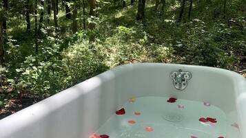 A bathtub filled with water and rose petals, surrounded by a forest.