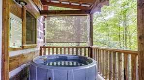 Ein Whirlpool auf einer Holzdielenterrasse mit Blick auf einen Wald.