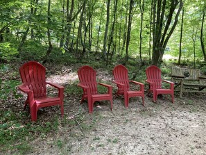Four red Adirondack chairs arranged in a row on a forest floor. - Beautiful Waterfront Cabin with Hot Tub near Winston-Salem, North Carolina (Elkin)
