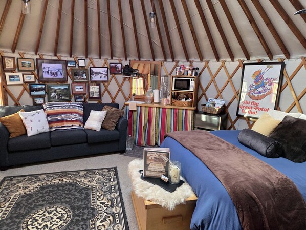 A cozy interior with a sofa, a bed, a small table, and a wall decorated with framed photos and a sign.