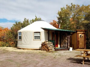 A yurt with a covered entrance, a stack of firewood, and a wooden door with a crescent moon symbol. - Secluded Cozy Yurt for Luxury Camping near Pocatello, Idaho (Pocatello)