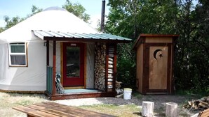 Una yurta con un porche, un banco de madera y una pequeña estructura de madera con una luna creciente y una estrella.