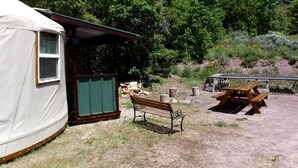 A rustic cabin with a wooden bench and picnic table, surrounded by dry grass and trees. - Secluded Cozy Yurt for Luxury Camping near Pocatello, Idaho (Pocatello)