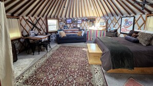 A yurt interior with a round ceiling, a sofa, a bed, a dining table, and a TV. - Secluded Cozy Yurt for Luxury Camping near Pocatello, Idaho (Pocatello)