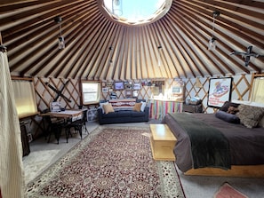A yurt interior with a round ceiling, a sofa, a bed, a dining table, and a TV. - Secluded Cozy Yurt for Luxury Camping near Pocatello, Idaho (Pocatello)
