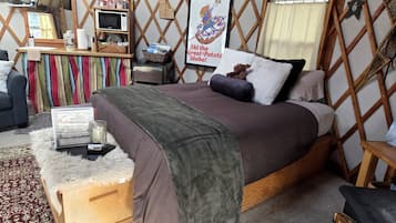 Een knus ingerichte kamer met een bed, een klein bureau, een magnetron en een poster aan de muur.