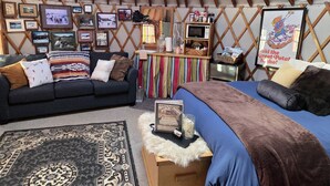 A cozy interior with a sofa, a bed, a small table, and a wall decorated with framed photos and a sign. - Secluded Cozy Yurt for Luxury Camping near Pocatello, Idaho (Pocatello)