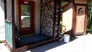 A small wooden structure with a red door, a covered porch, and a stack of firewood. - Secluded Cozy Yurt for Luxury Camping near Pocatello, Idaho (Pocatello)