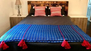 Un lit avec une couvre-lit à rayures bleues et des glands rouges, deux oreillers, une tête de lit en bois et une lampe de chevet.