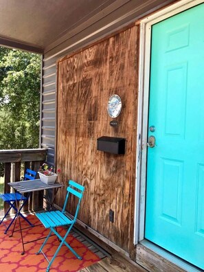 A wooden door with a mailbox, a blue chair, and a table with a potted plant on a porch.