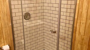 Une douche d’angle avec des portes en verre et des murs recouverts de carreaux blancs.