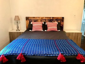 Una cama con colcha azul a rayas y flecos rojos, dos almohadas, un cabecero de madera y una lámpara de noche.