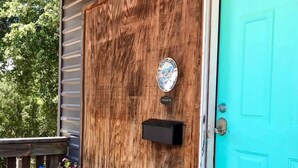 Une porte en bois avec une boîte aux lettres, une chaise bleue et une table sur laquelle est posée une plante en pot, le tout sur un porche.