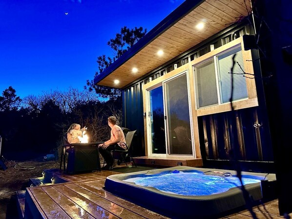 A hot tub with a wooden deck, a covered seating area, and a glass door leading to a room.
