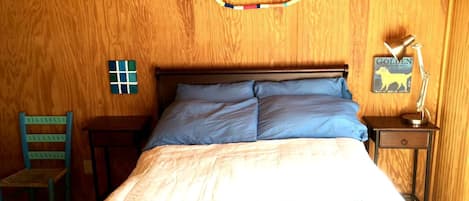 Ett rum med träpanel på väggarna, innehållande en säng, en stol, ett litet bord och en väggdekoration.