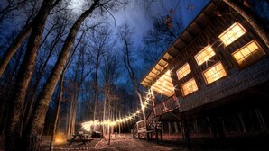 A rustic cabin with multiple windows, a deck, and a string of lights. - Tree House Glamping near Fall Creek Falls State Park and Chattanooga, Tennessee (Dunlap)