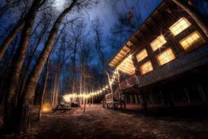 A rustic cabin with multiple windows, a deck, and a string of lights.