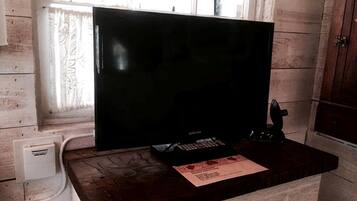 A room with a wooden desk, a black television, a Samsung box, and a window with patterned curtains.